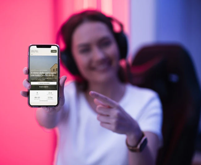 collaboratrice Wainet con cuffie seduta in ufficio mostra Iphone con Sito Web agriturismo appena realizzato
